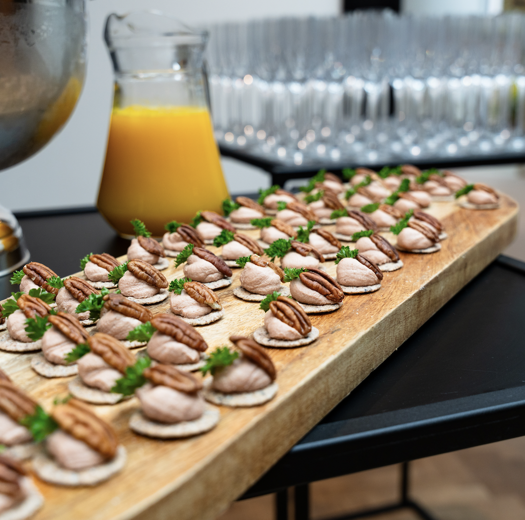 Fijne hapjes met mousse en pekannoot naast een karaf verse jus d'orange