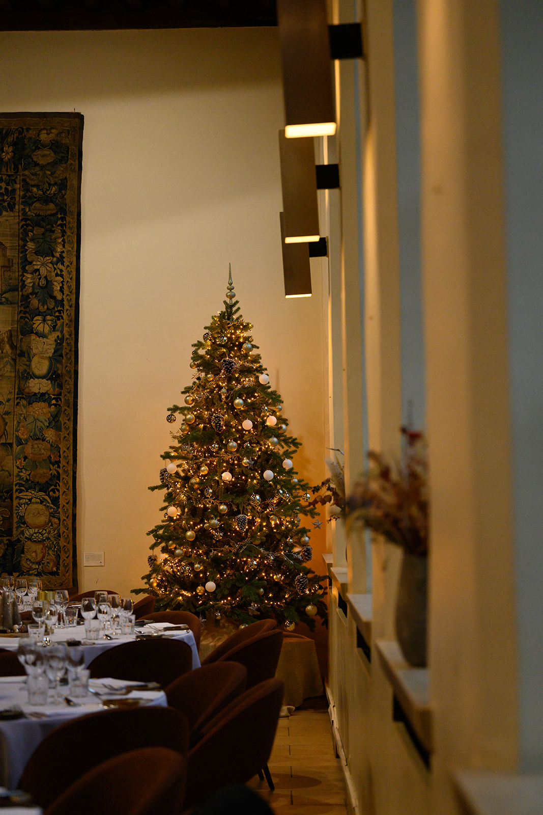 Verlichte kerstboom naast gedekte tafels in het restaurant van Priorij Corsendonk