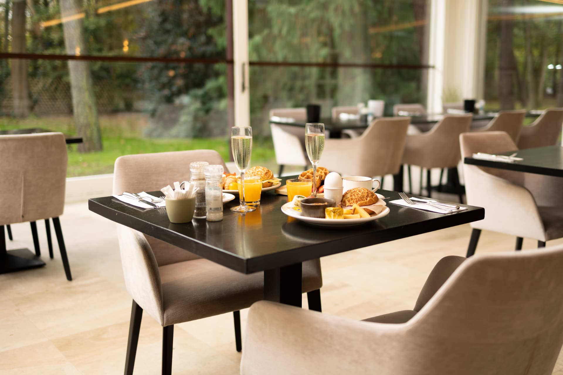 Gedekte ontbijttafel met cava, verse jus d'orange, wafels en broodjes bij het raam met zicht op de tuin