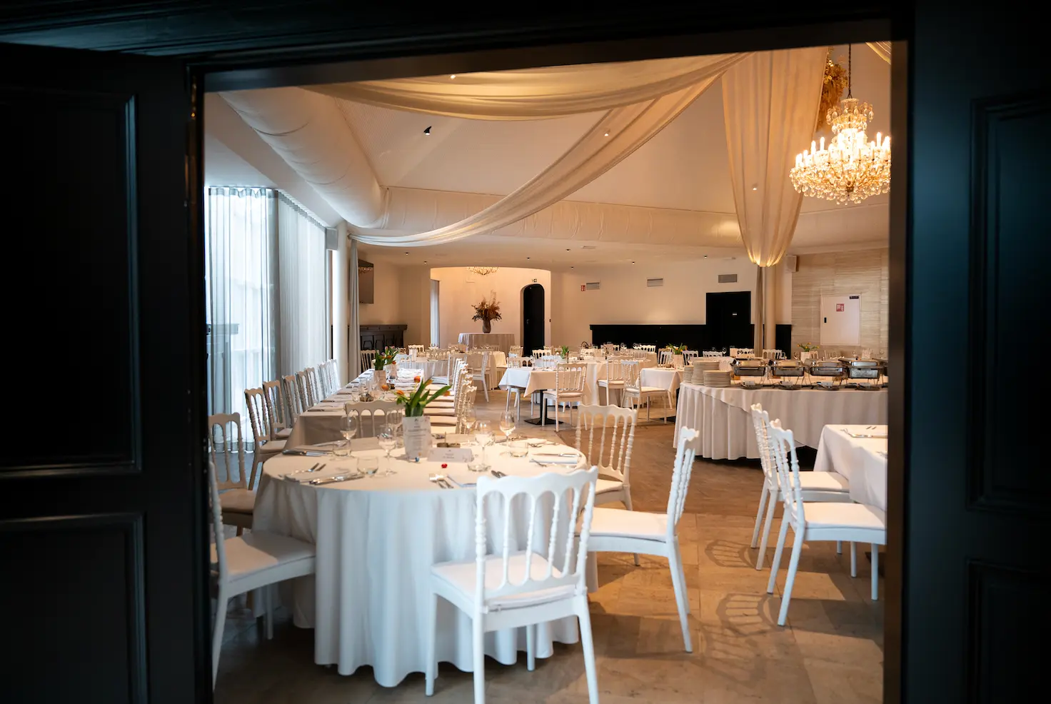 Doorkijk naar de feestelijk gedekte zaal met kroonluchter en witte tafels bij Corsendonk Hooge Heyde