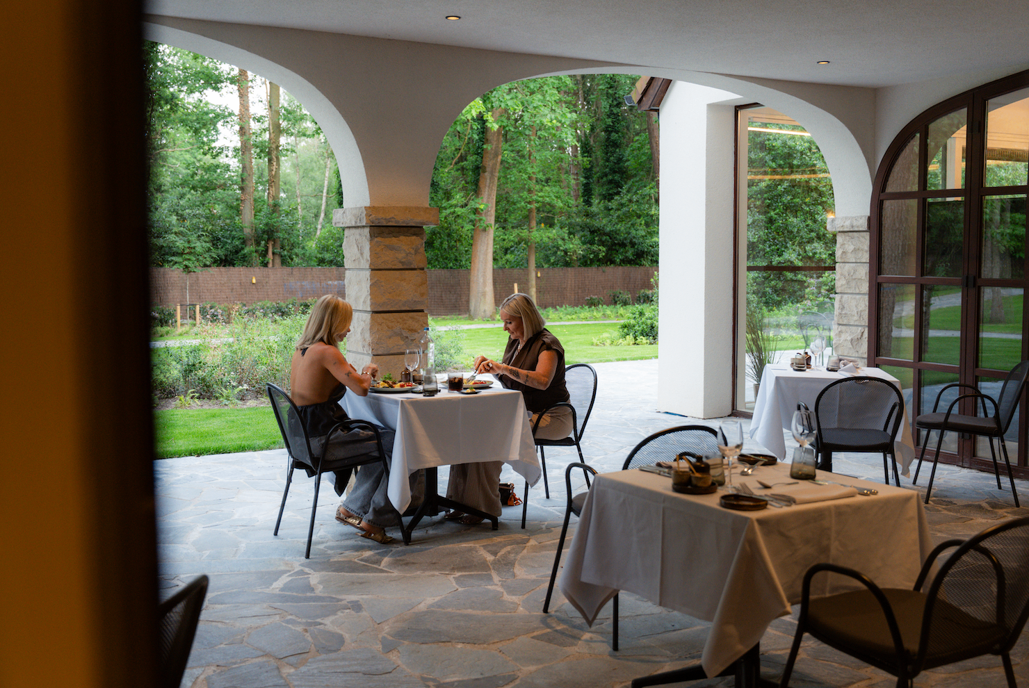 Gasten aan tafel onder de arcade met zicht op de tuin — Corsendonk Hooge Heyde